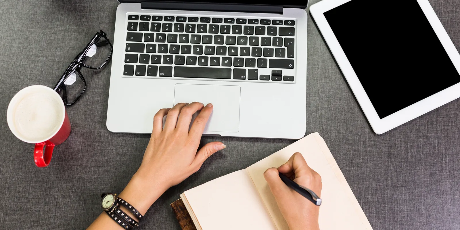 Arbeitsplatz mit Laptop, Tablet und Notizbuch von oben betrachtet