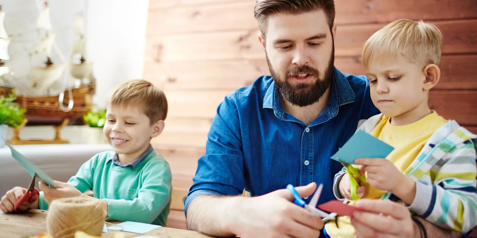 Pädagogischer Mitarbeiter bastelt mit zwei Grundschulkindern am Tisch