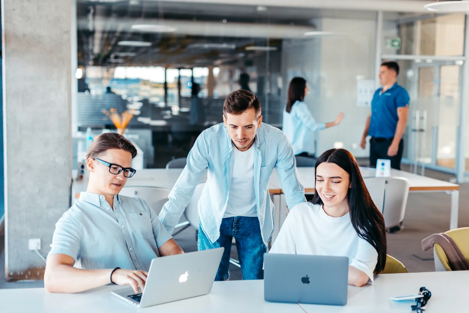 Drei Kolleg:innen arbeiten gemeinsam an Laptops im Büro