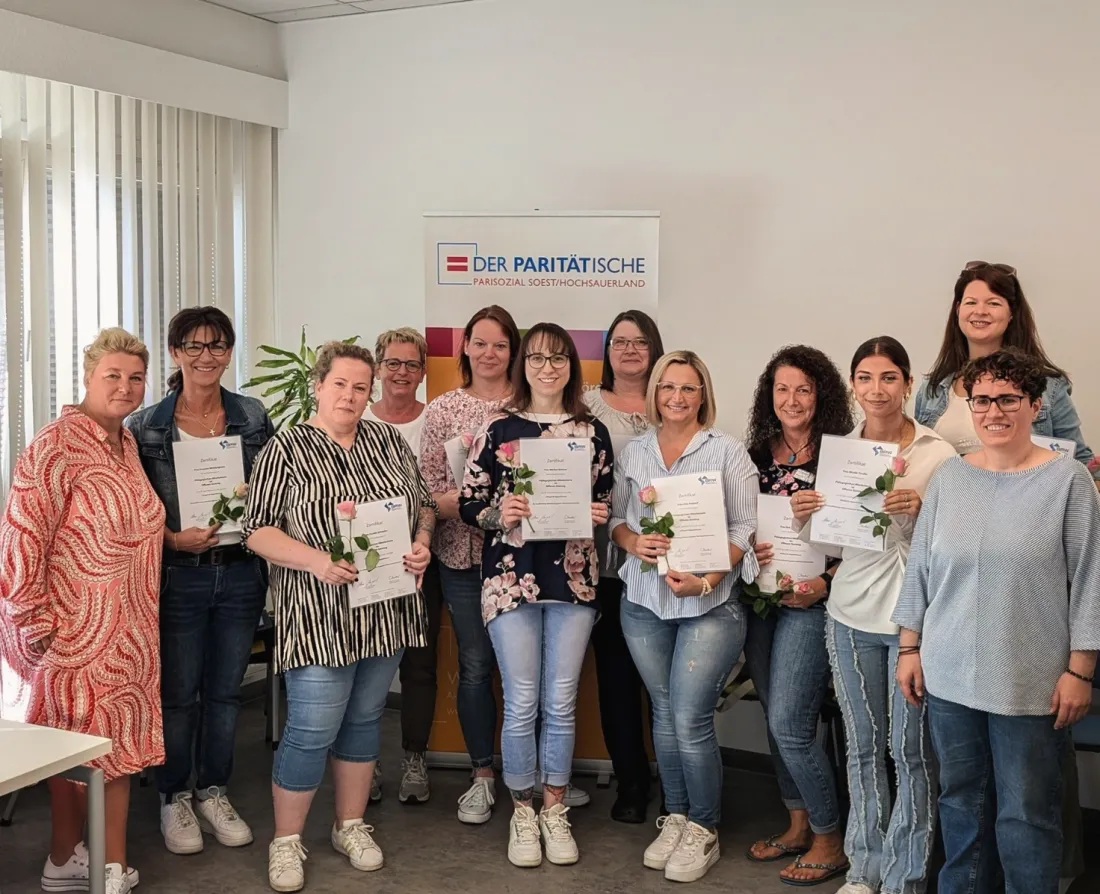 Absolventinnen einer Inhouse-Schulung mit ihren Zertifikaten vor einem Banner des Paritätischen Soest/Hochsauerland