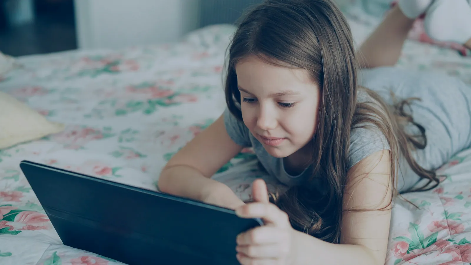 Grundschulkind liegt auf dem Bett und nutzt ein Tablet